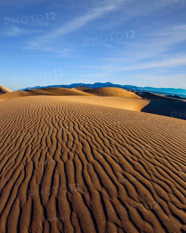The gentle slopes of the sand dunes are rippled by the wind. USA. Mesquite Flat Sand Dunes is a picturesque part of Death Valley in California. Concept of active, ecological and photo tourism