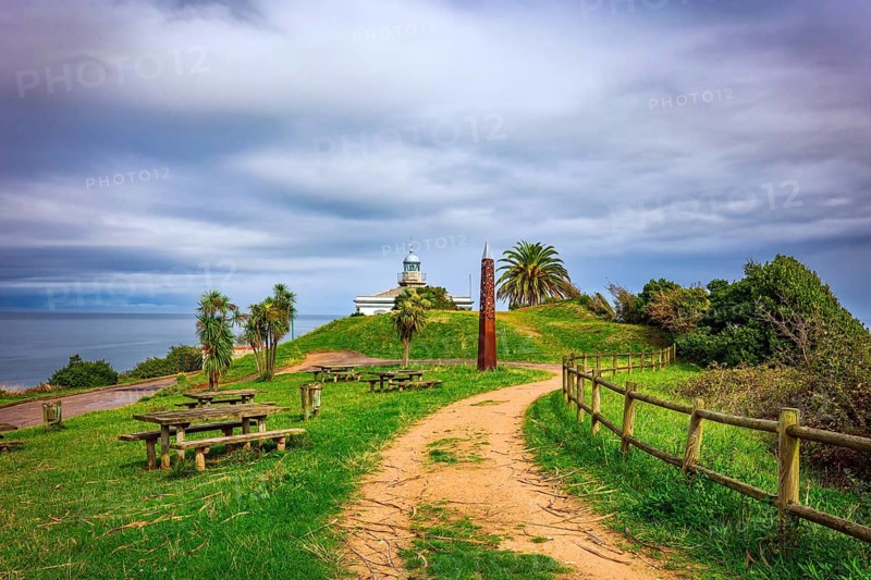 The road to the lighthouse. The picturesque seaside fishing town of Candas. Atlantic coast, Spain. Part of the famous Costa Verde beach. Snow-white lighthouse over the cliff