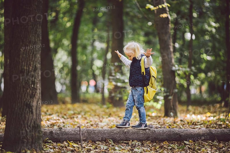 The theme children outdoor activities. Funny little baby Caucasian blond girl walks through forest overcoming obstacles, tree fell, log. Baby hiking big funny backpack in autumn forest park