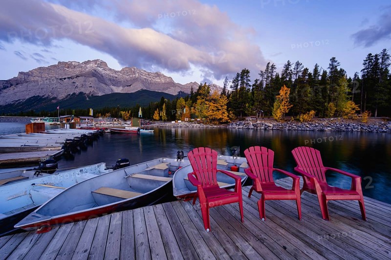 Beautiful autumn landscape scene in lake and mountain in background in west Canada, colour kayaks and canoes and small boats Three red plastic chairs