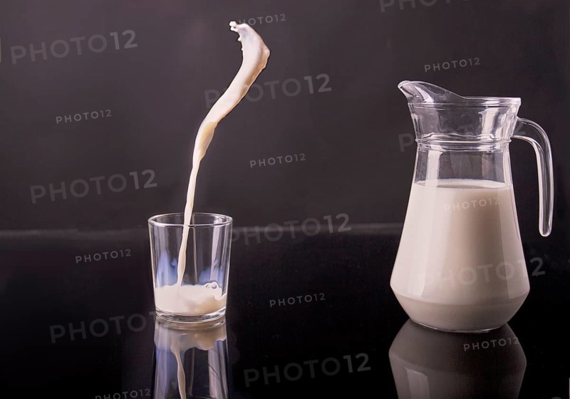 Glass jug and cup filled with white milk. Pouring organic drink in motion