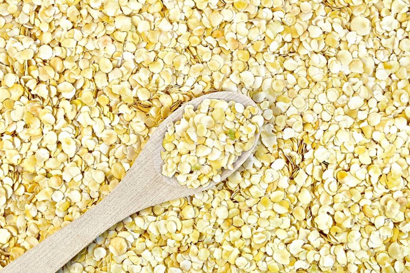 Texture of yellow pea flakes with a wooden spoon