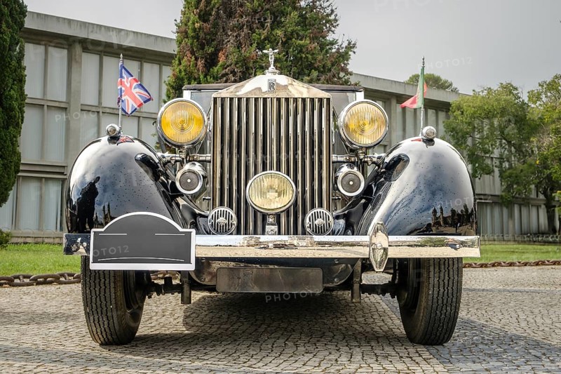Lisbon, Portugal - Oct 15, 2023: Front view of Rolls-Royce Phantom III parked in cobblestone driveway. Full-size luxury car, 1930s, by Rolls-Royce Ltd, Britain, UK. Portuguese and British flags, hood mascot, Spirit of Ecstasy, grille, big headlights