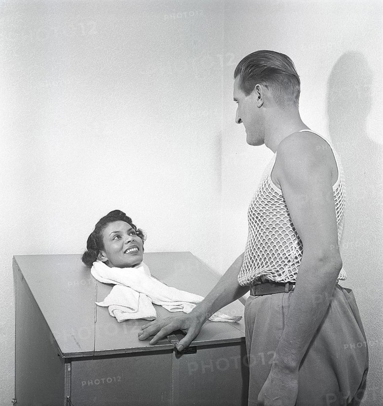 Beauty care in the 1950s. A young woman is sitting in a steam sauna, with only her head sticking up. A man handling the treatment is standing beside her. He is wearing the very special kind of sleeveless shirt with the fabric knitted as a net, mainly to be used under your shirt. Sweden 1951. Photo Kristoffersson Ref BE102-1