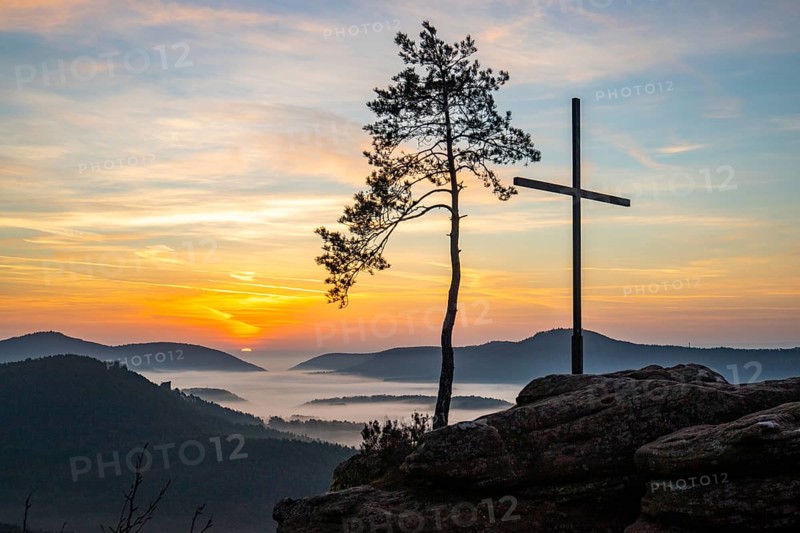 Landscape shot of nature in the morning. Mist in the valley and a summit cross on a sandstone cliff. Sunrise in the Palatinate Forest, Germany
