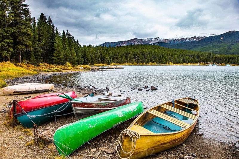 Multicolored boats and canoes dry on the lakeside. Cold cloudy fall day in the Canadian Rockies. Lake Maligne in the snow-capped mountains is surrounded by coniferous evergreen forests