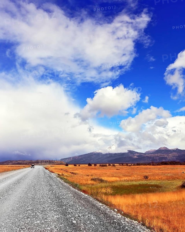 The dirt road in the endless pampas. Strong wind drives the clouds. See the mountains on the horizon
