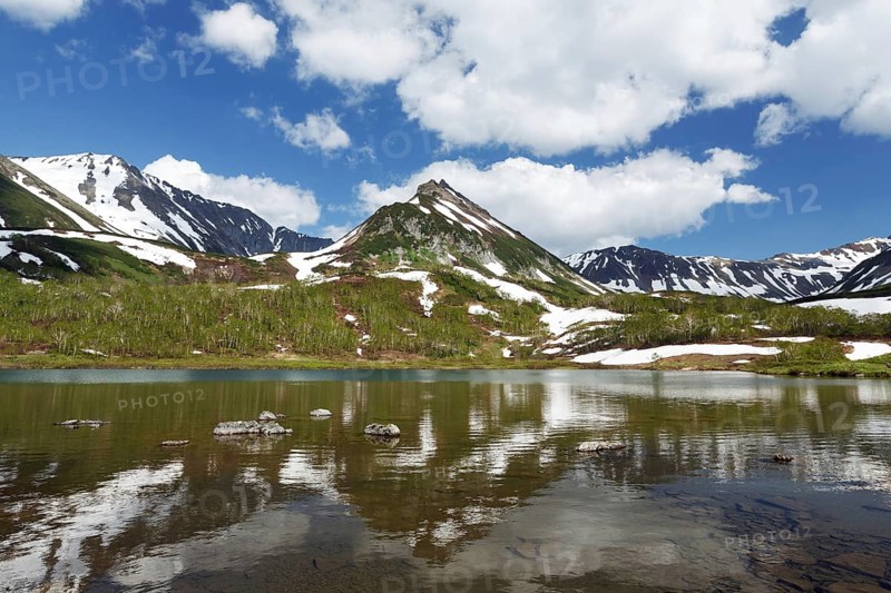 Summer landscape of Kamchatka: view of Mountain Range Vachkazhets and clouds in blue sky, reflection in mountain lake on sunny day. Eurasia, Russian Far East, Kamchatka Peninsula