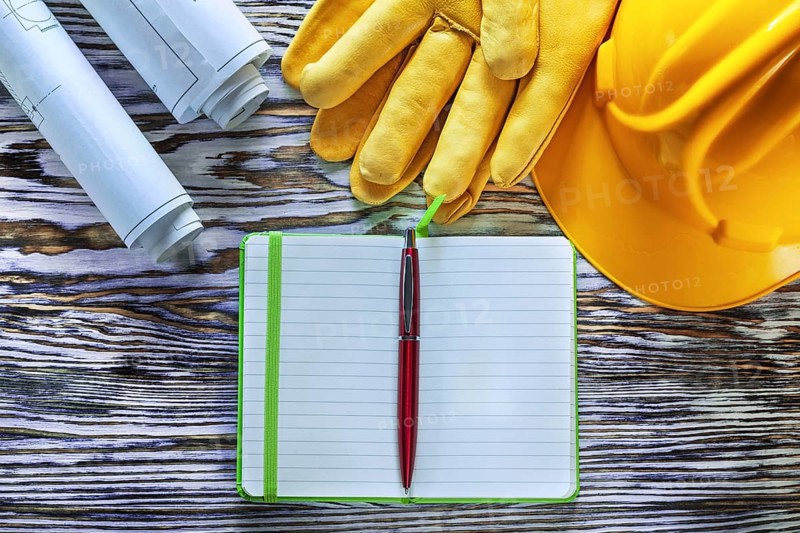 Blueprints notepad pen building helmet safety gloves on vintage wooden board