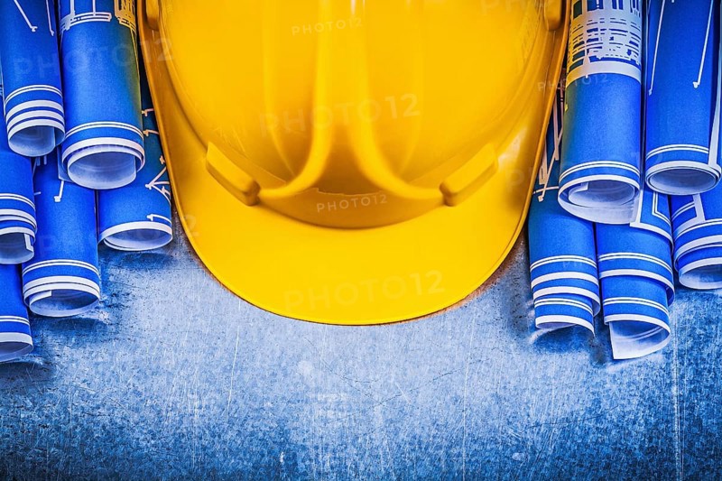 Blue rolled engineering drawings yellow building helmet on metallic background construction concept