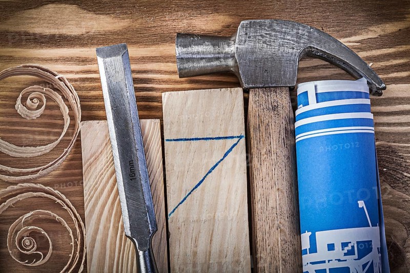Blue rolled construction drawing claw hammer firmer chisel wooden studs curled shavings on vintage wood board