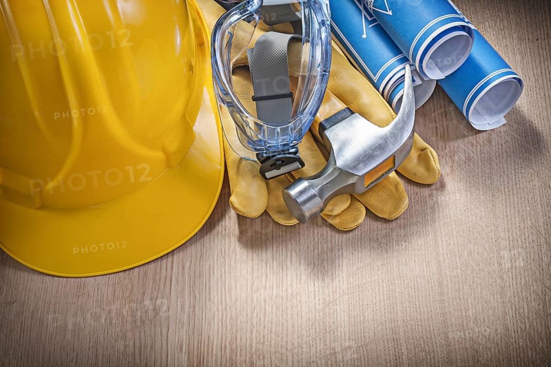 Protective work wear claw hammer rolled construction plans on wooden board