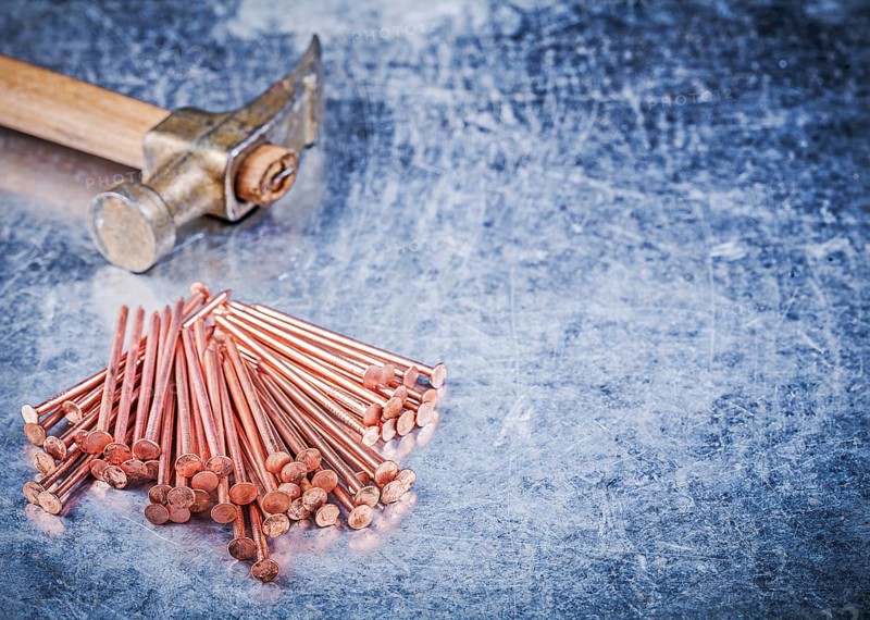 Vintage claw hammer heap of brass construction nails on metallic background