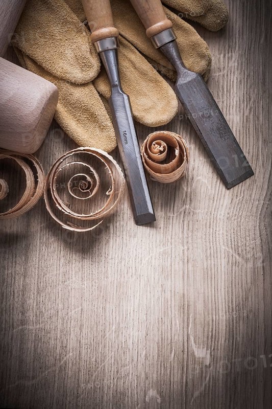 Wooden mallet curled up shavings flat chisels leather gloves on wood board vertical view construction concept