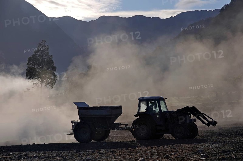Tractor spreading lime with a fertiliser spreader, West Coast, New Zealand