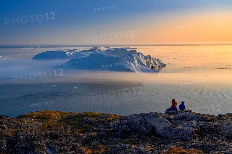 Large glaciers in the bay by the rocky shore in the light of the setting sun with fog over the water