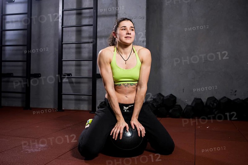 Theme sport and health. Strong muscular caucasian woman in the gym sitting on a black heavy padded fitball taking a break from a crossfit strength training in the gym