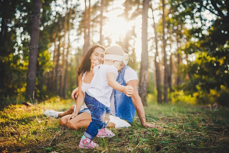 Young parents are taught to walk a daughter of one year on nature in a park on a lawn. The first steps of the child's hand with his mother and father