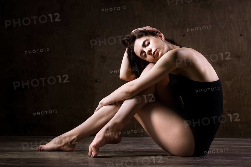 Beautiful young girl dancer with long flowing hair in black clothes, a gymnastic swimsuit, in a dance pose on a wooden floor with a dark background. Dance theme Contemporary and Classics
