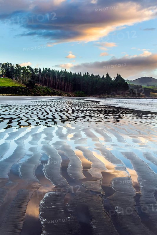 Sunrise over the ocean. Artistic postal and greeting card. Strips of sand and water left by the ocean tide. New Zealand, Pacific Coast. The concept of artistic photography