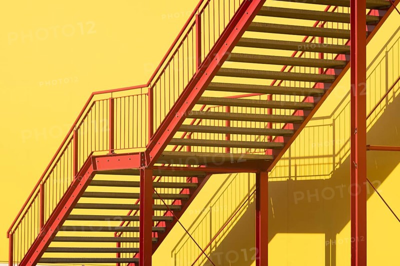 Red metal outdoor stairway in front of yellow wall