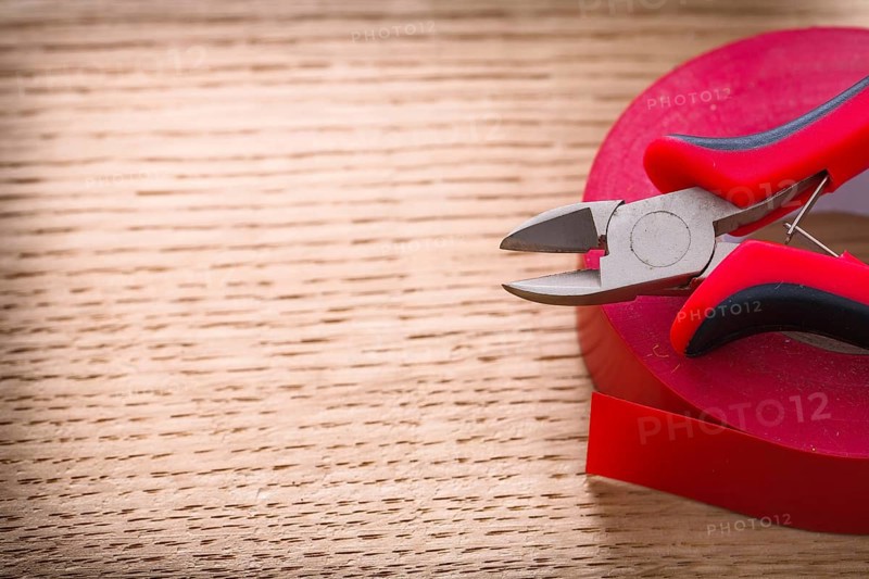 Red nippers and insulating tape on wooden board