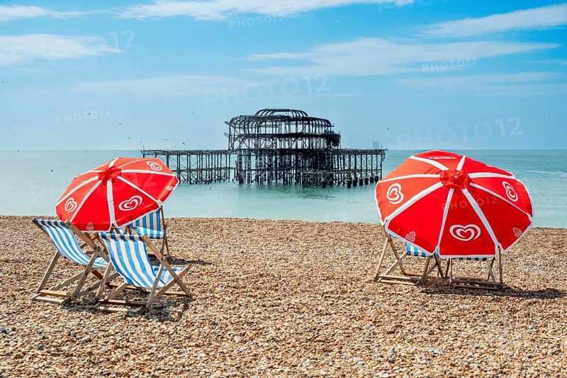 Folding chairs with parasols on the beach in front of the ruins of the burnt down West Pier in Brighton, East Sussex, England, Great Britain