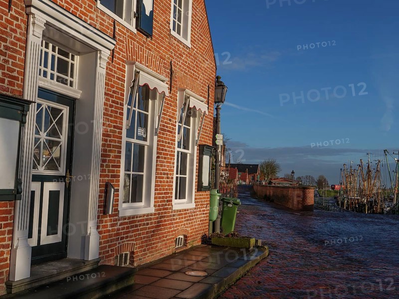 A sunny harbour street with brick houses and water in the background, Greetsiel, East Frisia, Germany
