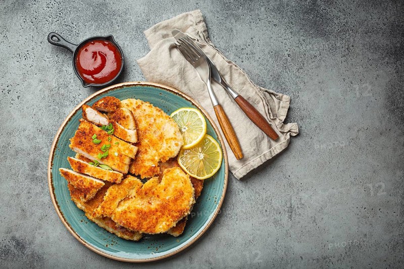 Crispy panko breaded fried chicken fillet with green salad and lemon cut on plate on gray background table with ketchup from above. Japanese style deep fried coated chicken breasts, space for text, food photography, food photography