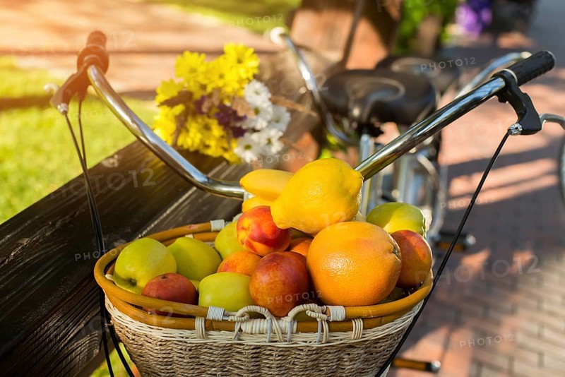 Basket filled with fruits. Bicycle near fence. Vitamins and energy of sun. Juicy apples and sweet peaches