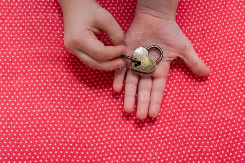 Hand holding a heart shaped lock and key on a red background