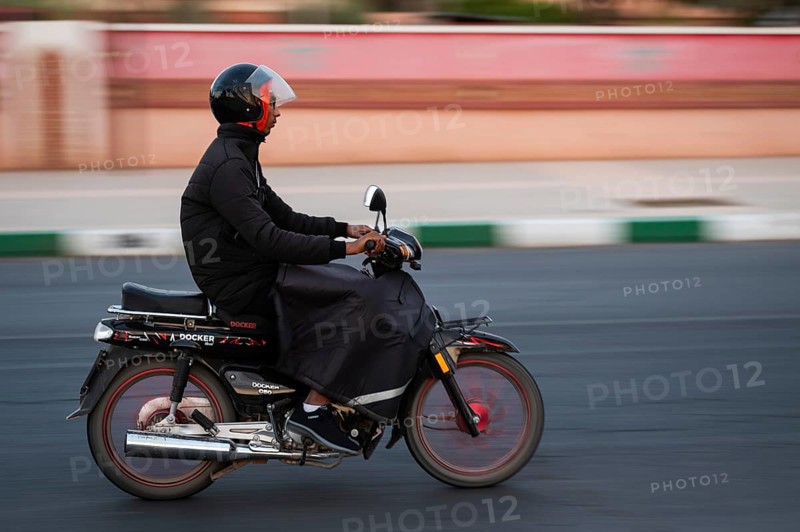 Marrakesh, MOROCCO - OCTOBER 5, 2024: Moroccan man riding a scooter on the road. Blurred background due to panning