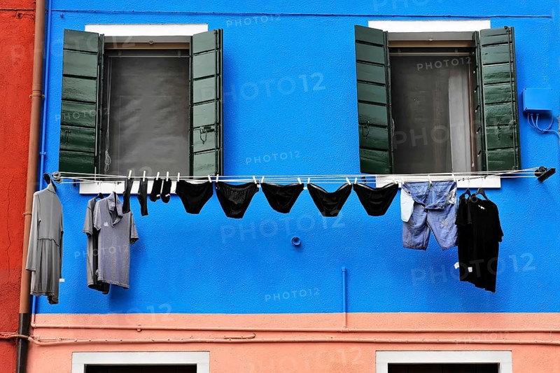 Venice, Veneto, Italy, Europe, Vibrant blue façade with green shutters, contrasting clothing on clothesline in foreground