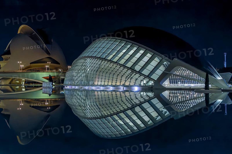 Night photo with illumination and spying on the water of the futuristic, unique and spectacular front part, modern architecture building L'Hemisfèric and in the background the cultural centre Palau de Les Arts Reina Sofía in the ultra-modern science complex in a landscape park Ciudad de las Artes y de las Ciencias, Quatre Carreres, Valencia, Autonomous Community of Valencia, Province of Valencia, Spain