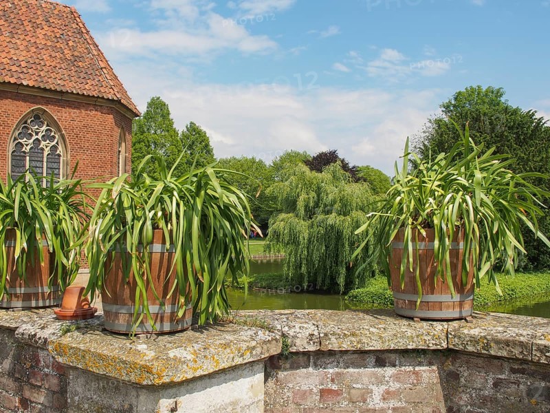 Flower pots on a brick wall in front of a historic building with gothic window and green backdrop, Havixebeck, münsterland, germany