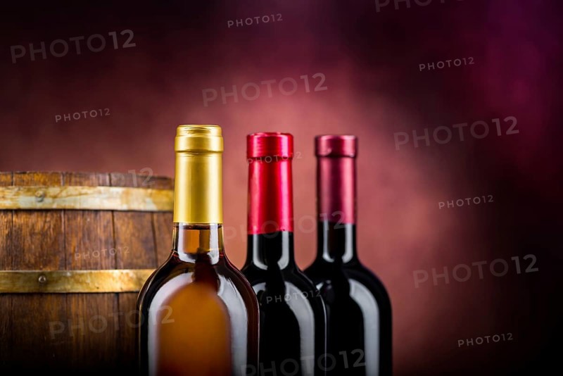 Three bottles of wine and wooden barrel on a burgundy background