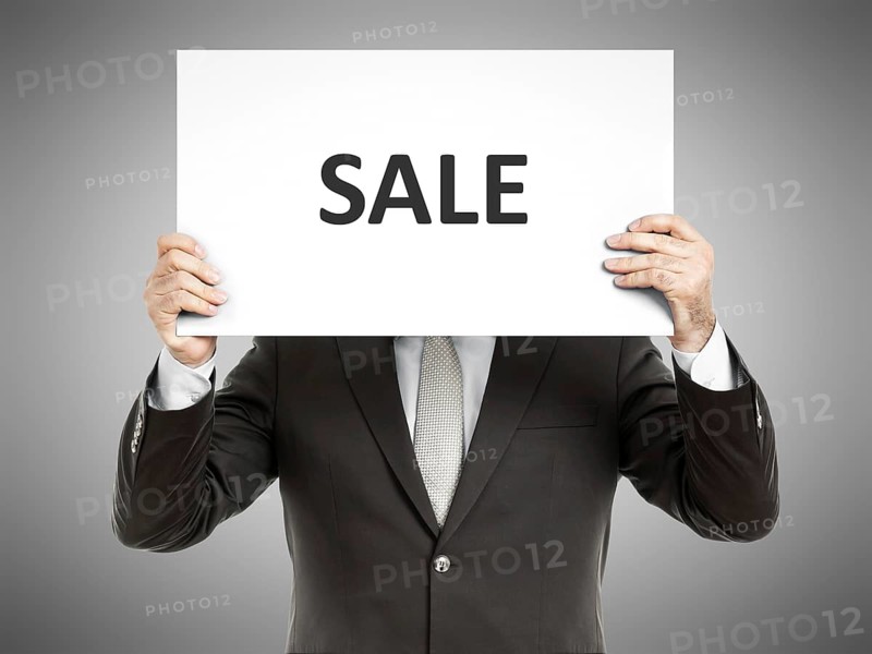 A business man holding a paper in front of his face with the text sale