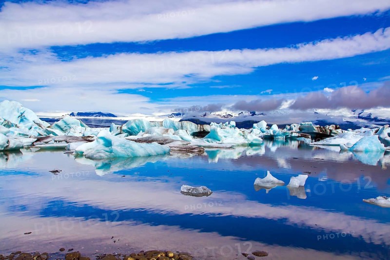 Clouds reflected in the smooth water of the largest glacial lagoon Jokulsaurloun. Iceland. Cold early summer morning. White and blue icebergs and ice floes. The concept of northern and photo tourism