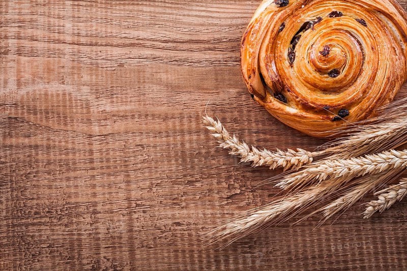 Sweet raisin bun bunch of wheat ears on oak wooden board food and drink concept