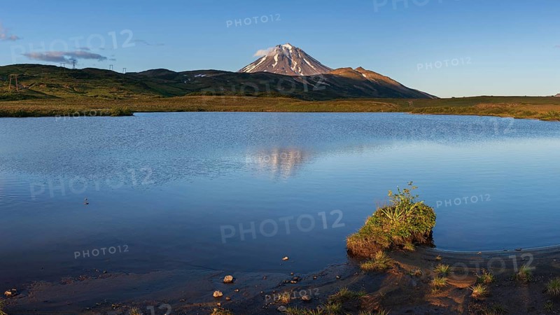Stunning evening panoramic mountainous landscape of Kamchatka Peninsula at sunset: scenery autumn view of cone Vilyuchinsky Volcano, reflection of mountains in alpine lake. Russian Far East, Eurasia