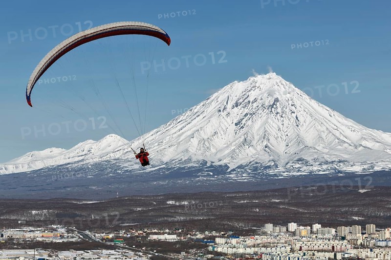 PETROPAVLOVSK-KAMCHATSKY, KAMCHATKA, RUSSIA, NOVEMBER 21, 2014: Paraglider flying over Petropavlovsk-Kamchatsky City on the background of the active Koriaksky Volcano on a sunny day