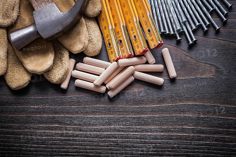 Wooden meter heap of dowels claw hammer leather protective gloves and metal nails on vintage wood board horizontal view construction concept