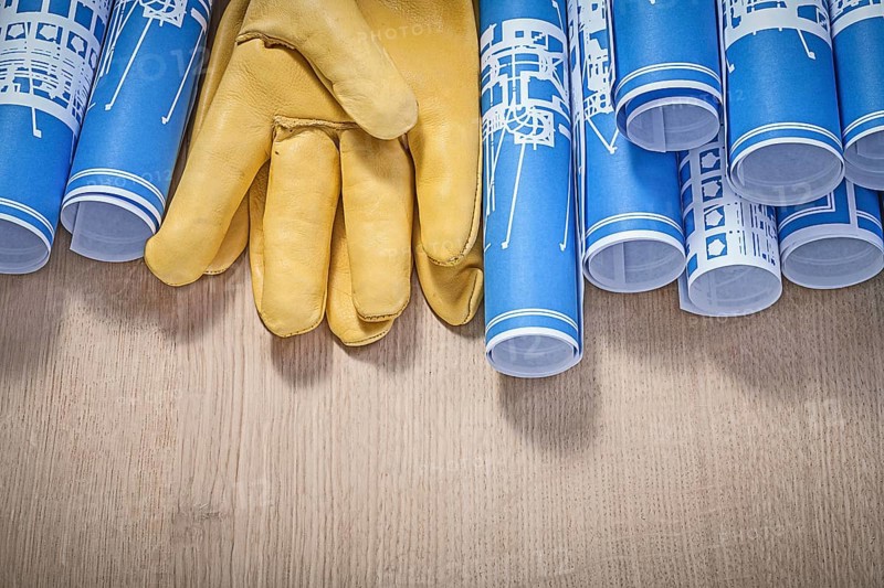 Blue rolled up construction plans leather protective gloves on wood board