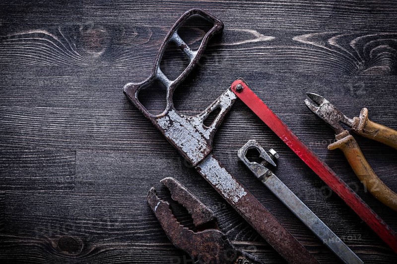 Obsolete vintage handsaw wire-cutter pliers on wooden board construction concept