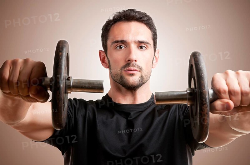 Personal Trainer doing front dumbell raises for training his deltoids in a brown background