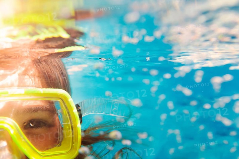 Little girl in colorful swimming mask smiling looking at camera under water