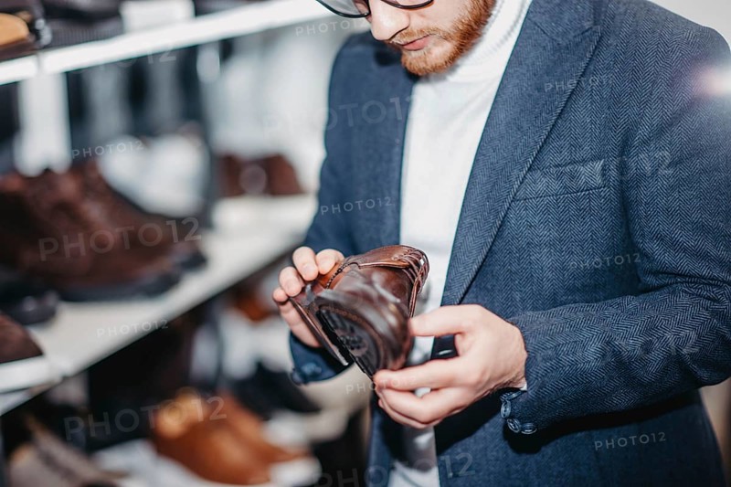 A man inspects a brown leather shoe on a store shelf