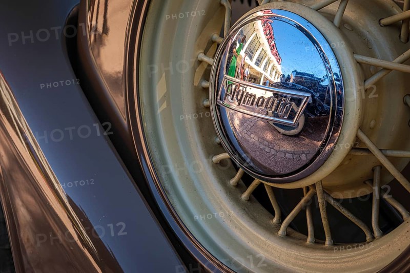 Lisbon, Portugal - Sep 29, 2024: Close-up and selective focus of spare wire wheel and wheel center cap with Plymouth logo on sunny day. Urban setting reflections, vintage look. Plymouth Chrysler motors, Chrysler Corp, USA