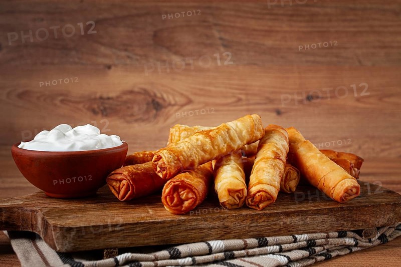 Fried spring rolls with cheese, on a wooden chopping board, with cream sauce, no people