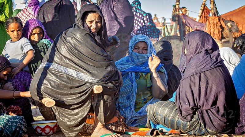 Gathering of people in colourful, traditional clothing in a desert landscape, woman at the traditional Tuareg festival of Tamanrasset in the Sahara in Algeria